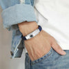 Black and blue plaited microfibre leather medical alert bracelet with silver stainless steel adjustable tag worn on a man wearing a denim shirt, jeans and white t-shirt.
