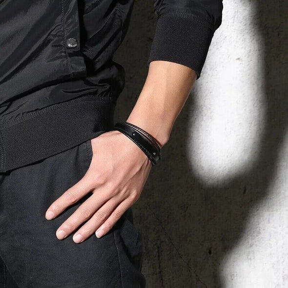 Dementia microfibre leather and stainless steel medical alert awareness bracelet worn by a man in black in front of concrete wall.