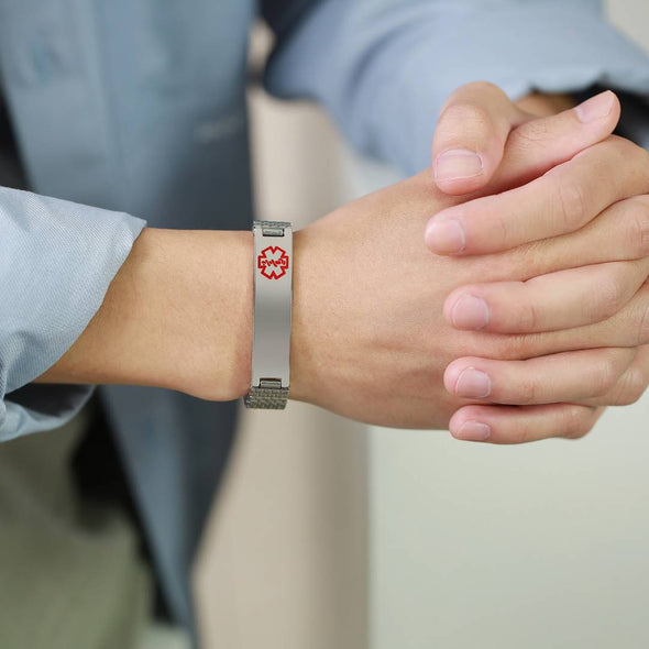 Stainless steel stretch medical alert bracelet on a man's wrist in blue long-sleeved shirt.