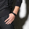Black multi-layered leather strap medical alert bracelet, blank version on a male model wearing black in front of a concrete wall